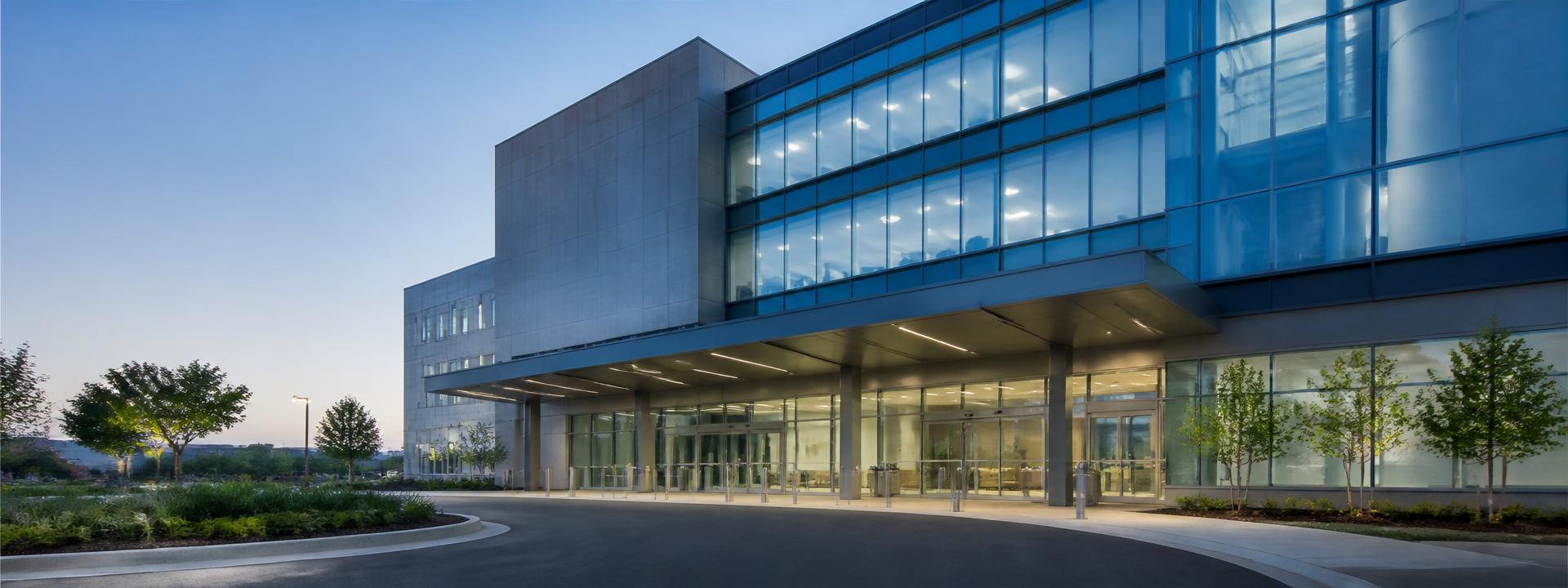 Modern hospital building exterior with a covered entrance canopy at dusk