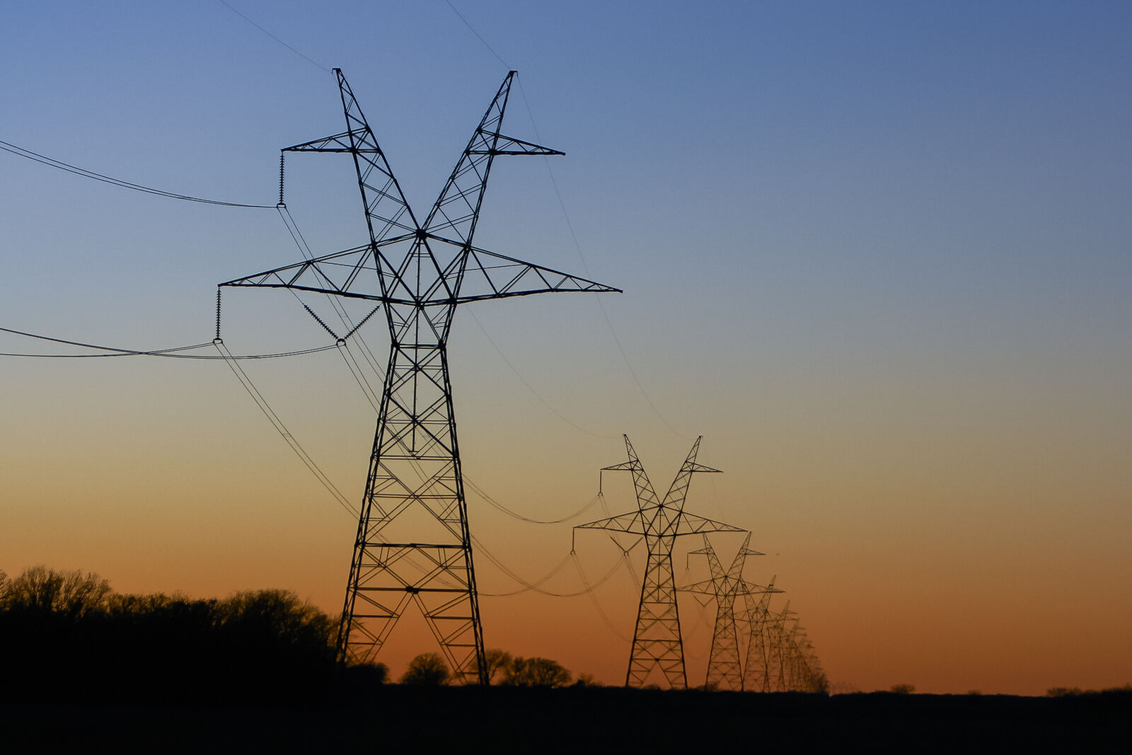 High-voltage electricity transmission towers silhouetted at sunset
